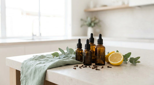 Amber glass dropper bottles with eucalyptus, cloves and a lemon on a pale stone benchtop, soft natural light, sage-mint 
